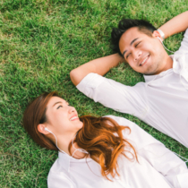 Young Asian lovely couple or college students lying down on the grass together, listening to music, top view with copy space. Love, relationship, wedding, or relaxing casual lifestyle concept